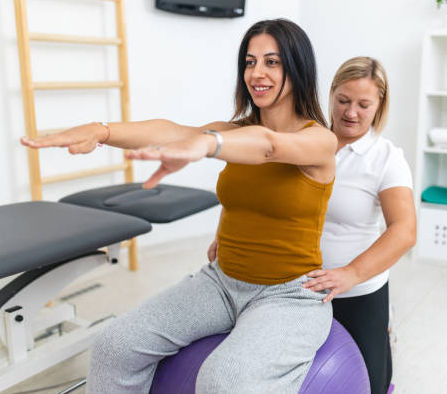 Bone Fit Therapy A professional female physical therapist helps a patient with rehabilitation exercises using a stability ball in a medical clinic setting. The focus is on recovery and promoting a healthy lifestyle.