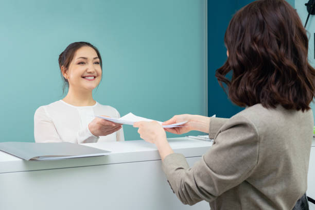 Receptionist accepts documents from the female visitor.