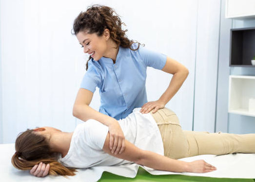 Young woman doctor chiropractor or osteopath fixing lying womans back with hands movements during visit in manual therapy clinic. Professional chiropractor during work